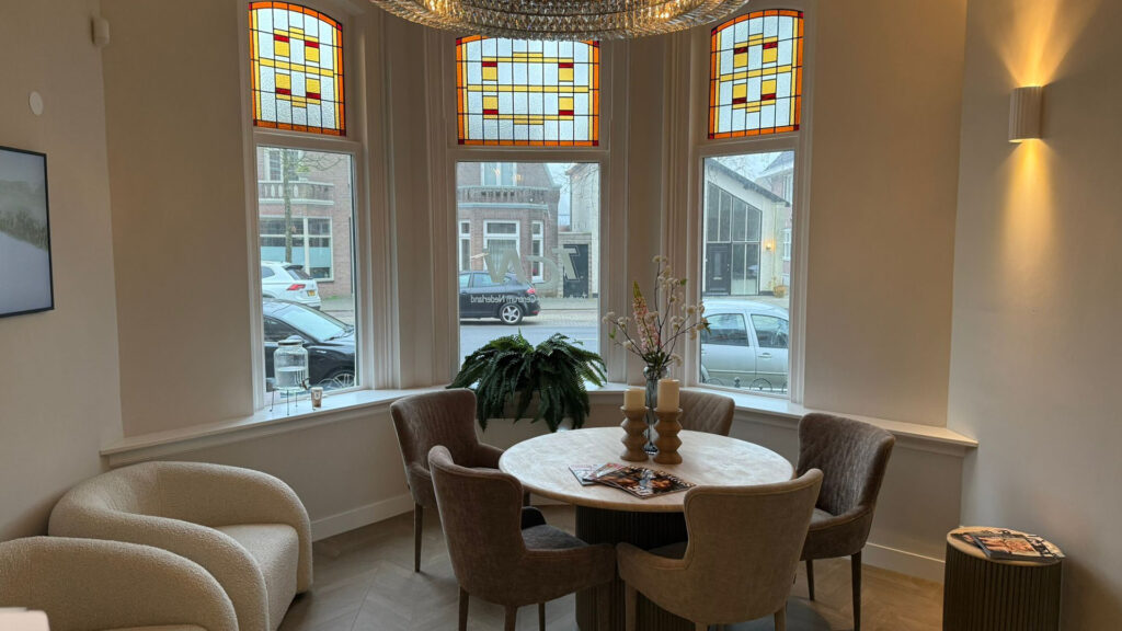 Wachtruimte met ronde tafel, stoelen en glas-in-loodramen bij Tandarts Alkmaar Centrum