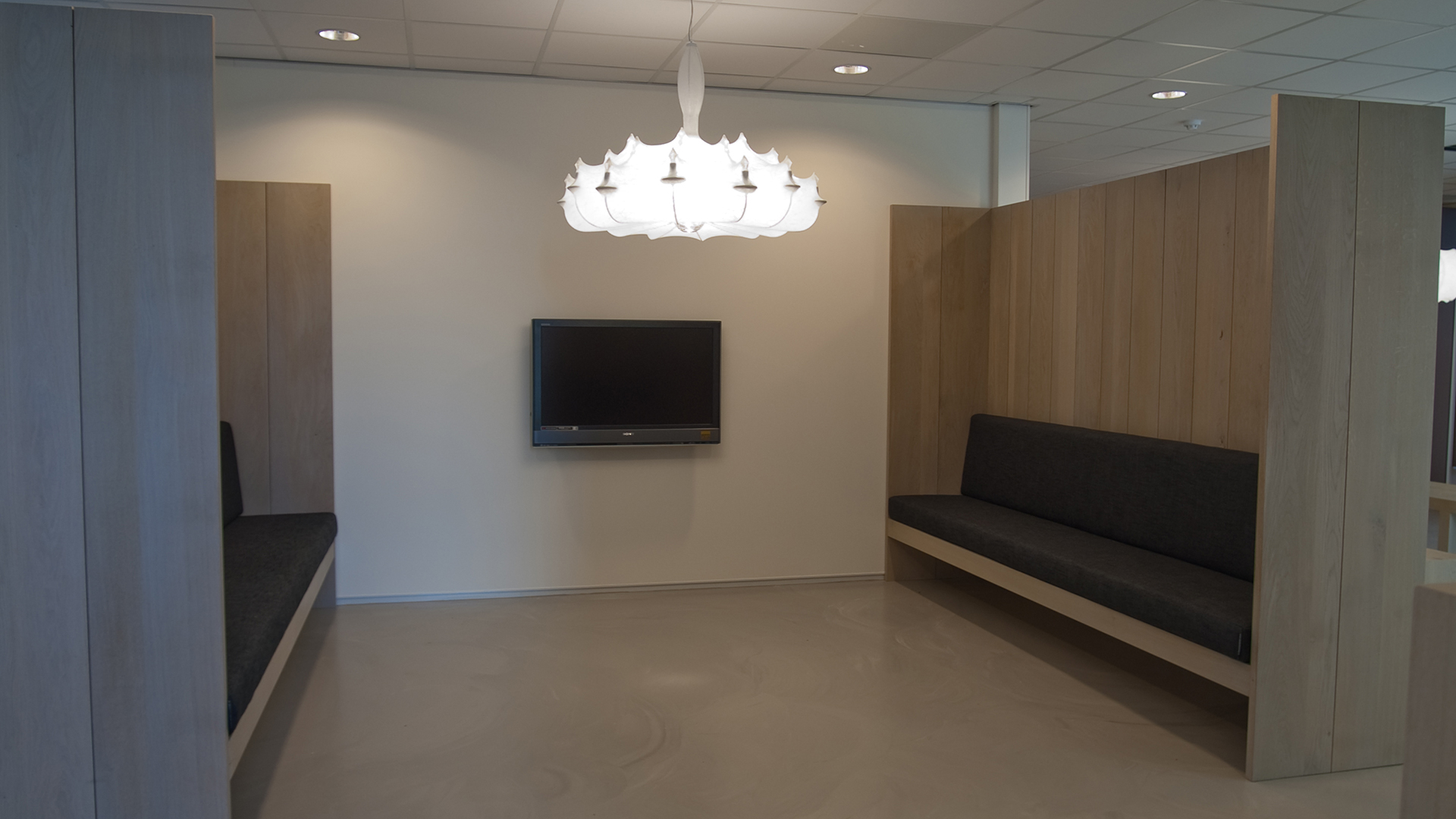 Wachtruimte met houten banken, kroonluchter en tv bij Tandarts Alkmaar Oudorp