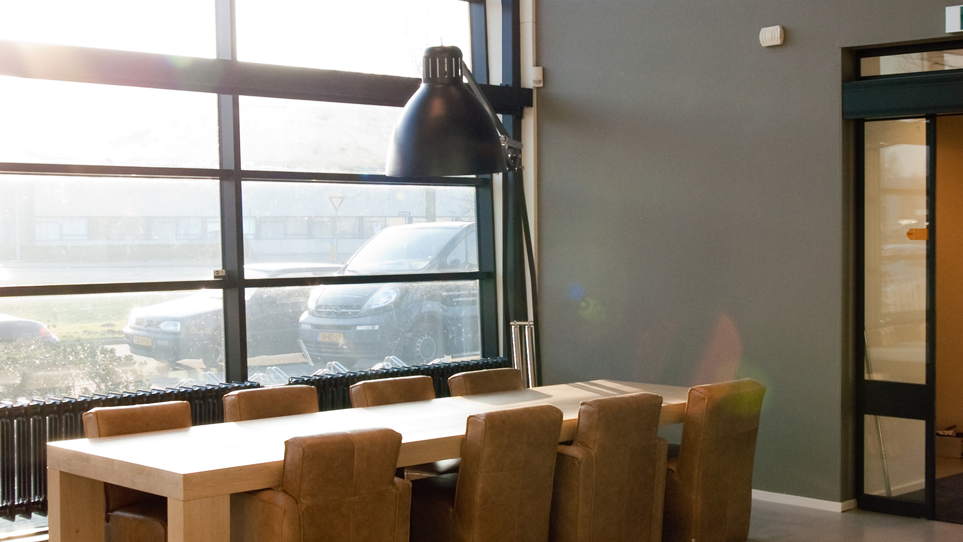 Vergadertafel met leren stoelen voor groot raam met zonlicht bij Tandarts Alkmaar Oudorp
