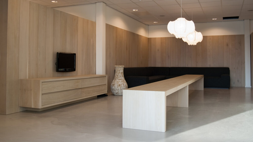 Gezellige wachtruimte met houten tafel, bank en hanglampen bij Tandarts Alkmaar Oudorp