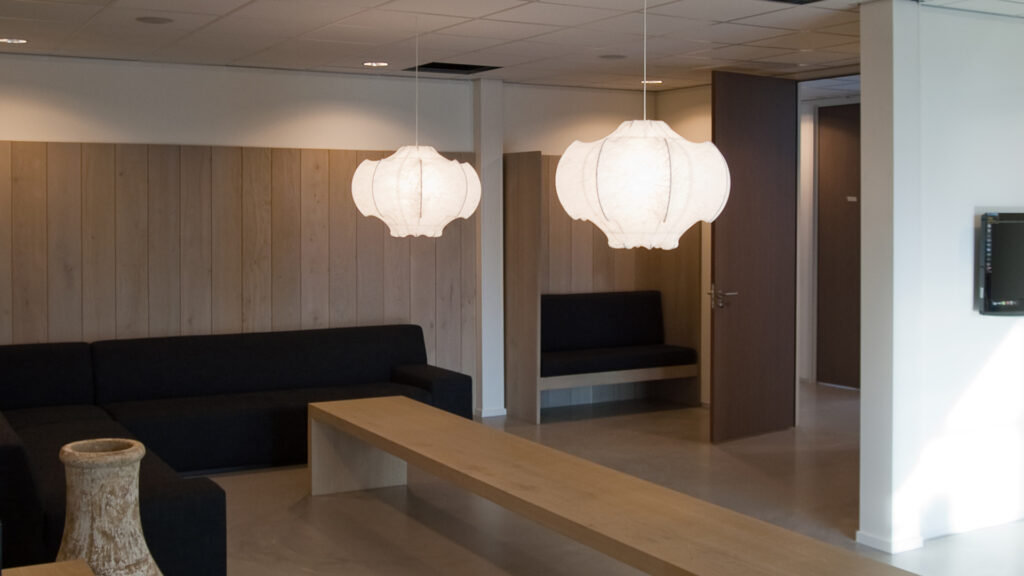 Moderne wachtruimte met houten wand, zwarte hoekbank en lange houten tafel bij Tandarts Alkmaar Oudorp