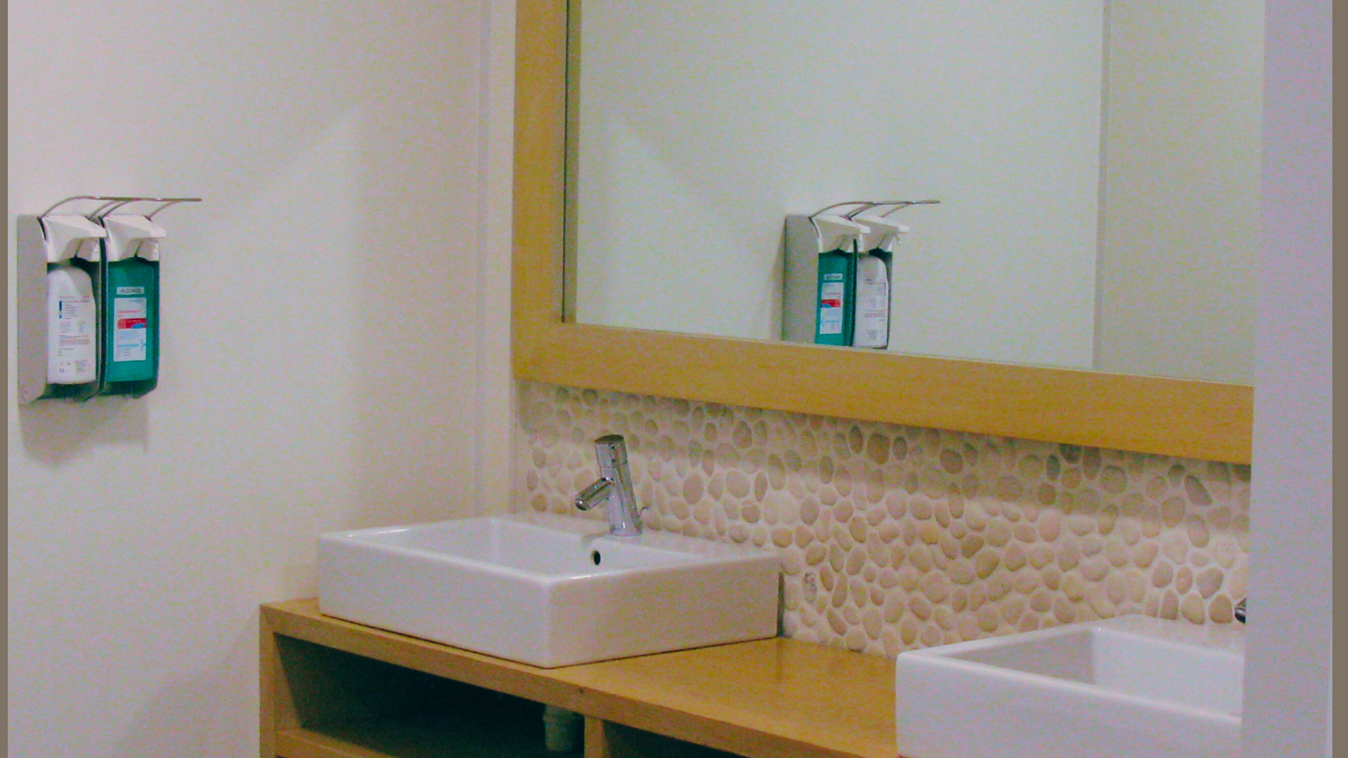 Wastafel met spiegel, houten blad en zeepdispensers bij Tandarts Alkmaar Oudorp