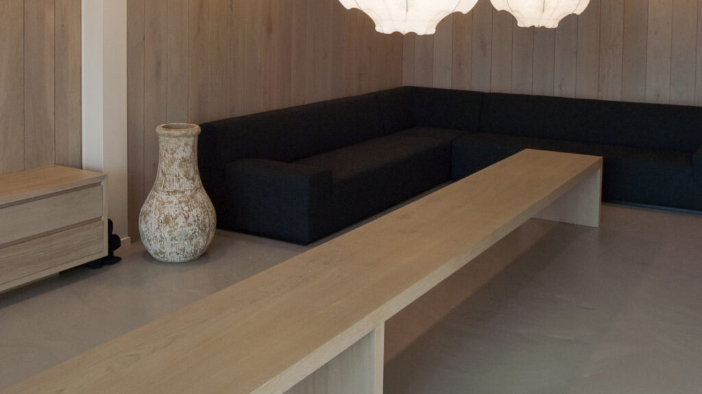 Zijkant van zithoek met houten tafel, vaas en zwarte hoekbank bij Tandarts Alkmaar Oudorp