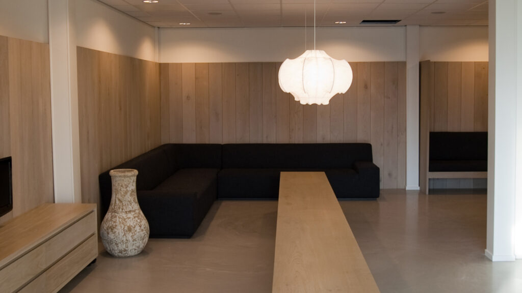 Gezellige zitruimte met zwarte bank en houten wandbekleding bij Tandarts Alkmaar Oudorp