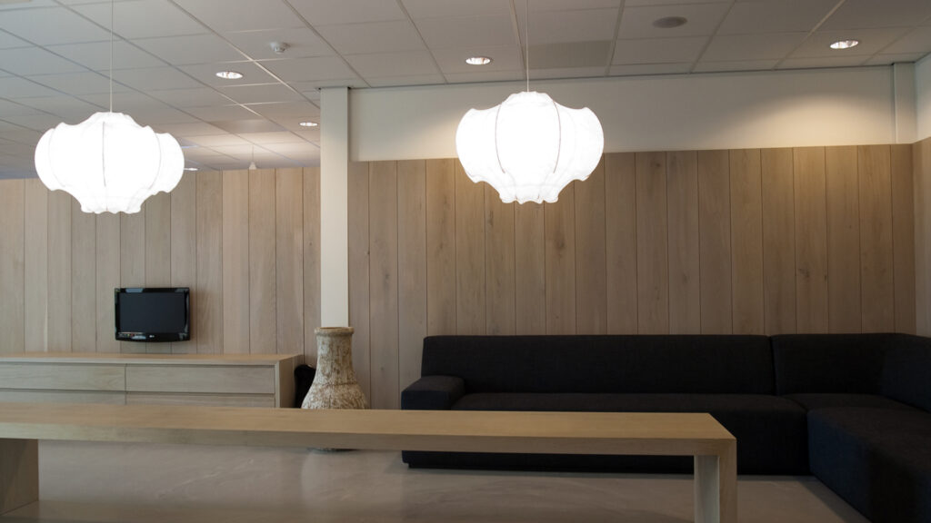 Lange houten tafel met hanglampen in zitruimte bij Tandarts Alkmaar Oudorp