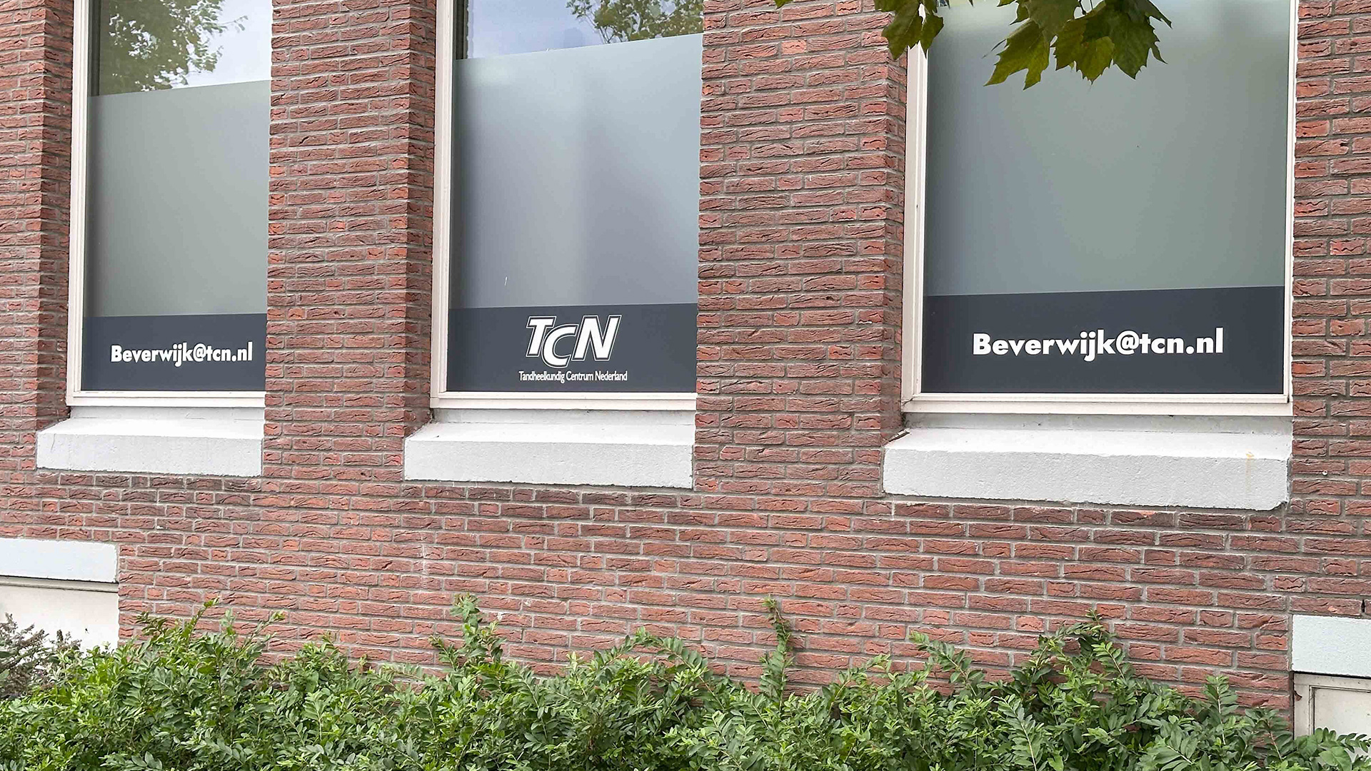 De raambestickering van de zijkant van het pand van TCN Beverwijk met contactinformatie