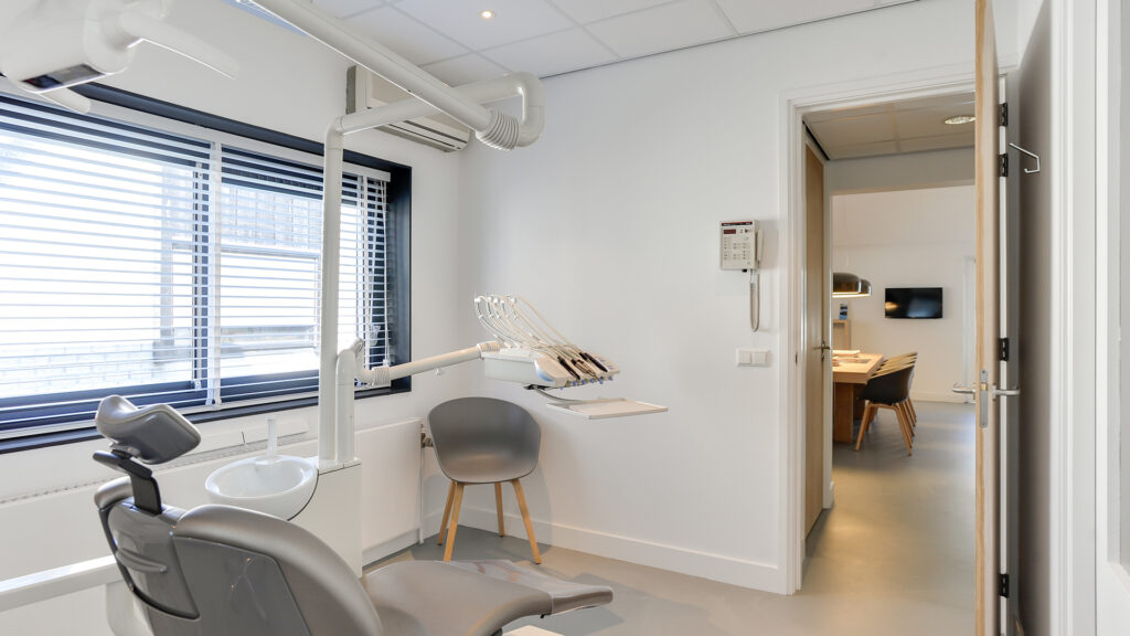 Behandelruimte met tandartsstoel en vergaderruimte op de achtergrond bij Tandarts Heerhugowaard