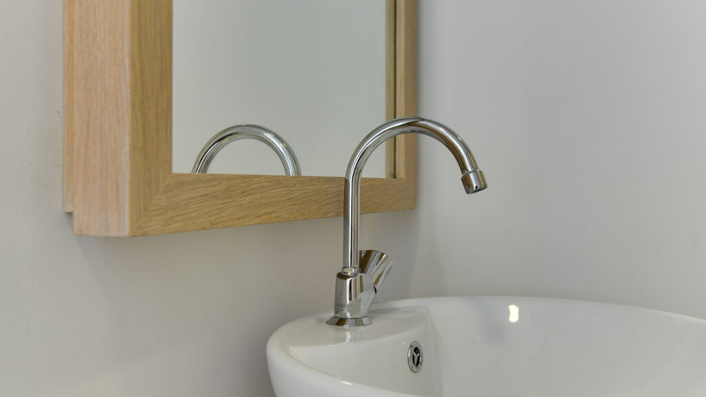 Close-up van wastafel met chromen kraan en houten spiegel bij Tandarts Heerhugowaard