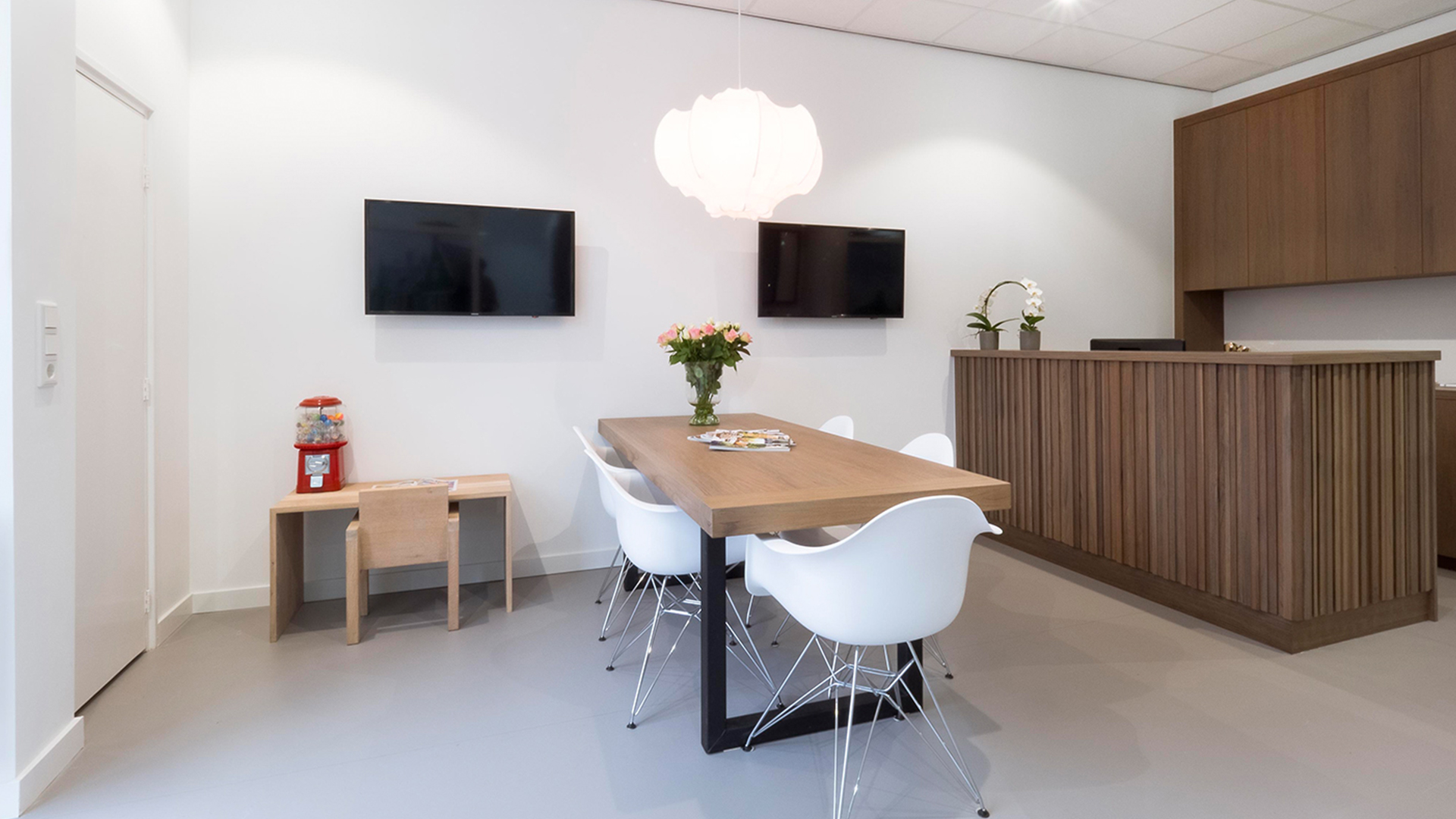 Wachtkamer van Tandarts Westzaan met houten tafel, bloemen en zicht op behandelruimtes