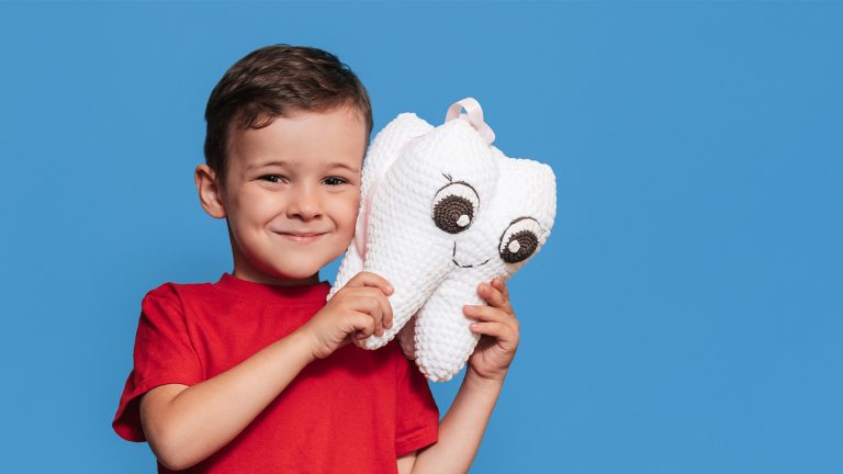Jongen in rood shirt houdt knuffel in de vorm van een lachende tand vast