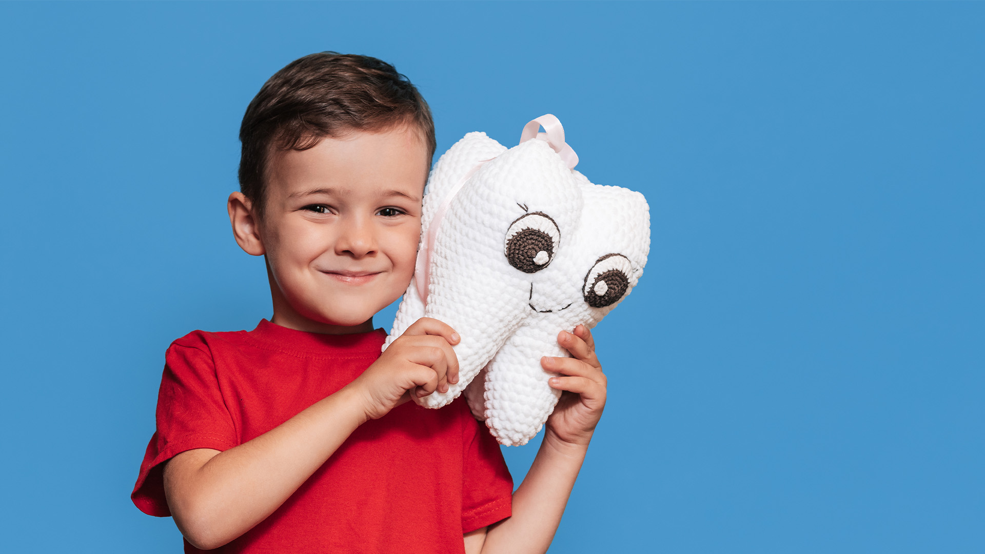 Jongen in rood shirt houdt knuffel in de vorm van een lachende tand vast