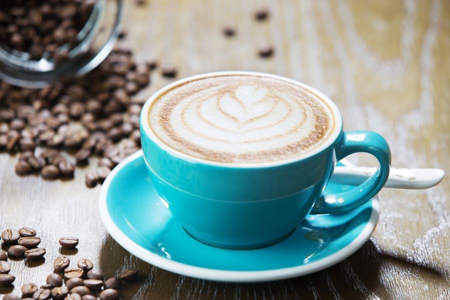 Blauwe koffiekop met cappuccino schuim en koffiebonen