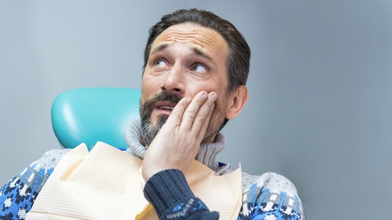 Man met baard die gespannen kijkt en zijn kaak vasthoudt in de tandartsstoel – Tandheelkundig Centrum Nederland