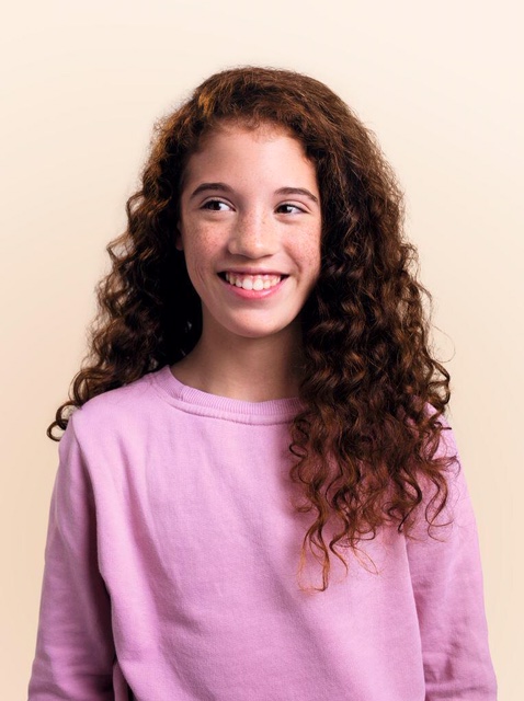 Meisje met krullend haar glimlacht en toont tanden na orthodontie voor kinderen