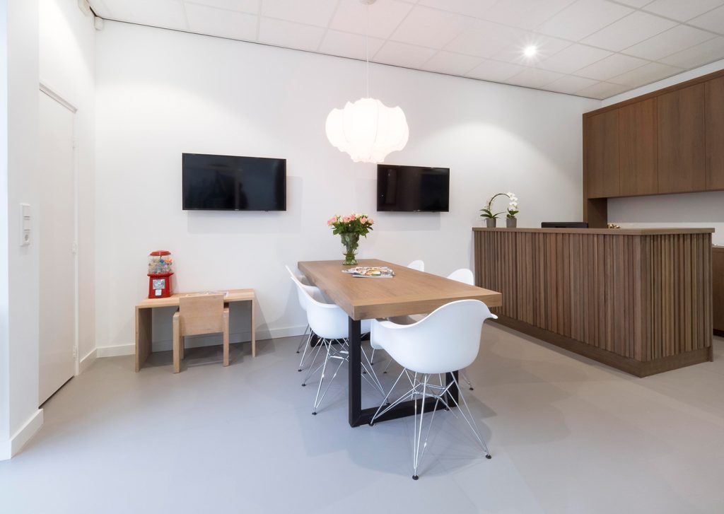 Wachtkamer van Tandarts Westzaan met houten tafel, bloemen en zicht op behandelruimtes