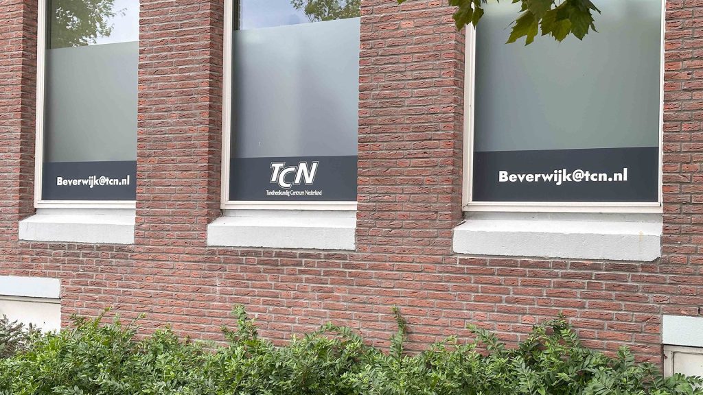 De raambestickering van de zijkant van het pand van TCN Beverwijk met contactinformatie
