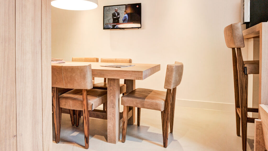 Zitruimte met houten tafel, leren stoelen en tv in wachtruimte bij Tandarts Castricum