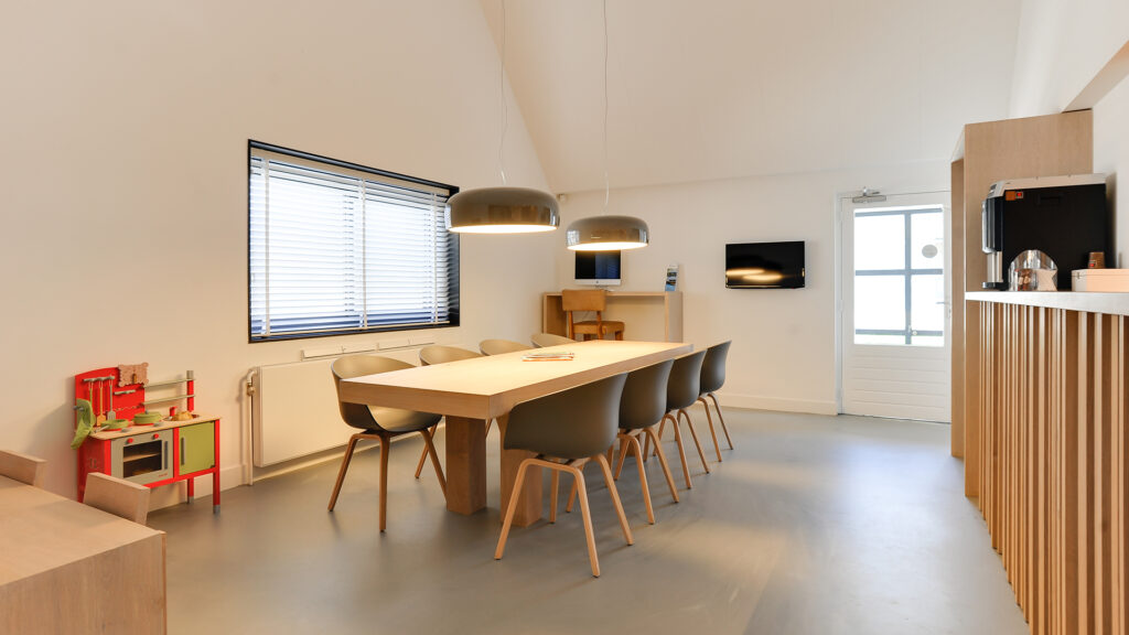 Wachtruimte met lange houten tafel, kinderhoek en koffiemachine bij Tandarts Heerhugowaard