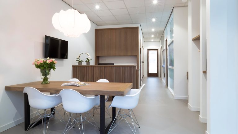 Wacht- en zitruimte bij Tandarts Westzaan met houten tafel, bloemen en moderne balie